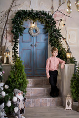  The child is smiling near the New Year tree. Happy child near the stairs. Stylish boy