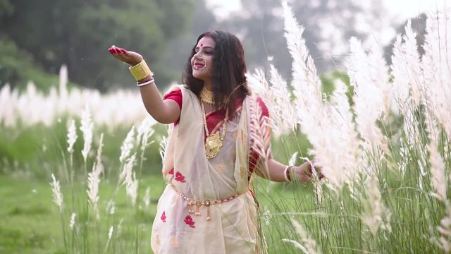 An innocent and playful married Indian bengali woman wearing saree plays with the long white grass in a field before durga puja or poyla boisakh, Gold jewelery. Slow motion