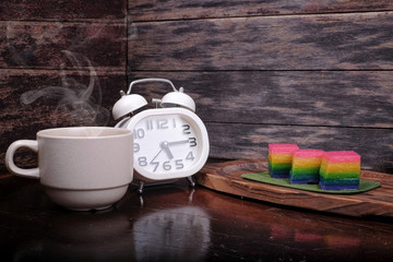 Traditional Malaysian food. Kuih Lapis , alarm clock and  a cup of coffee on wooden background....