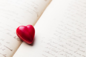 Chocolate heart shaped candy on vintage book with hand writing. Copy space.