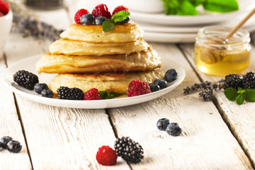 Pancakes with forest fruits berries on white table.