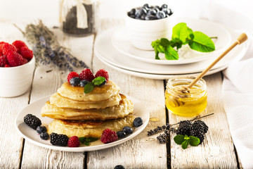 Pancakes with forest fruits berries on white table.