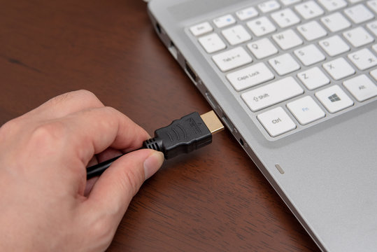 Man is connecting black hdmi cable into laptop.