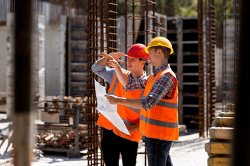 Structural engineer and construction manager in orange work vests and hard helmets explore...