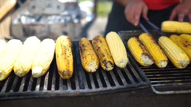 Close up of appetizing grilled sweet corn on the bbq grill. Street food festival. Shef turn the corn on grill.