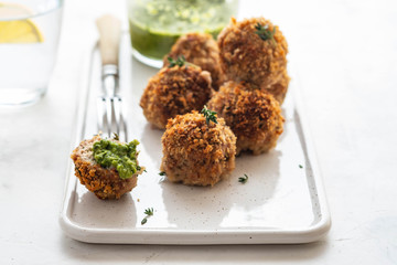 Homemade meatballs with thyme and green sauce on a white plate on white background.