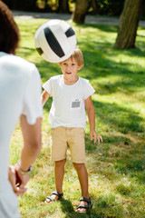 Summer time little boy dressed in the white t shirt is looking forward at the football ball flying in front of him.