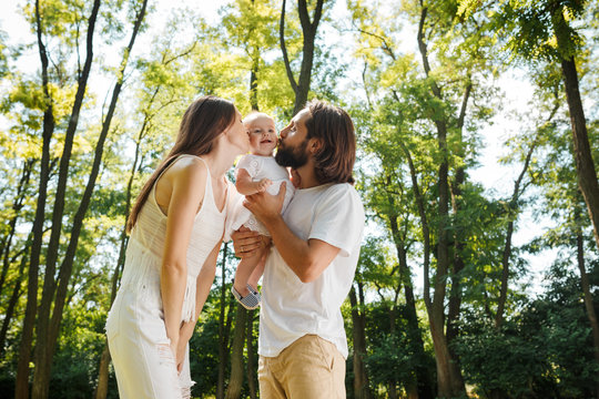 Happy family on the open air. Young dark-haired woman and her husband are kissing their charming little daughter.
