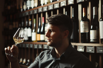 Sommelier looks at white wine in glass in cellar