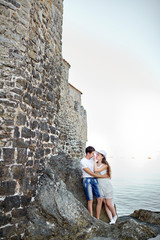 Couple in love hugging on the rocks against the background of an old stone wall, sea water and blue sky. Engagement portrait