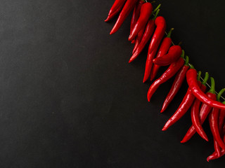Red hot spicy chili pepper on the black background.  A row of red hot chili peppers hanging.