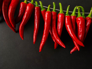 Red hot spicy chili pepper on the black background.  A row of red hot chili peppers hanging.