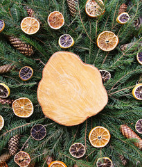 Wooden slice on green fir-tree branches decorated with dried orange slices and cones. Christmas and New Year vintage winter holiday festive composition.