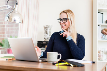 Portrait of smiling woman at her desk looking at laptop