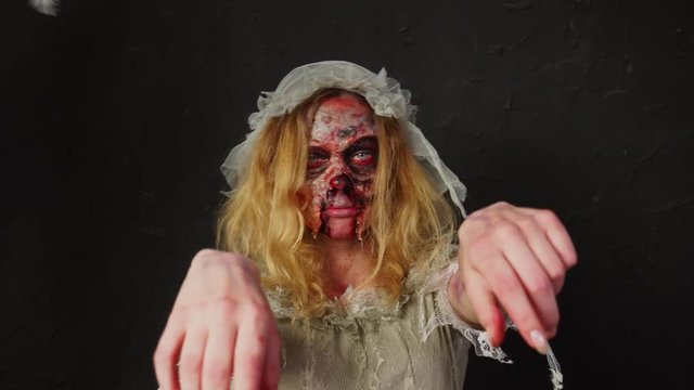 Professional zombie makeup for Halloween on young attractive blonde woman dead bride wife in dirty ripped wedding dress
