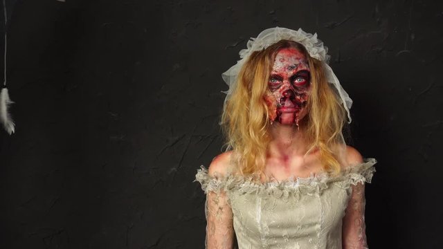 Horrifying young blonde woman wearing professional Halloween zombie makeup dead wife bride in dirty ripped wedding dress