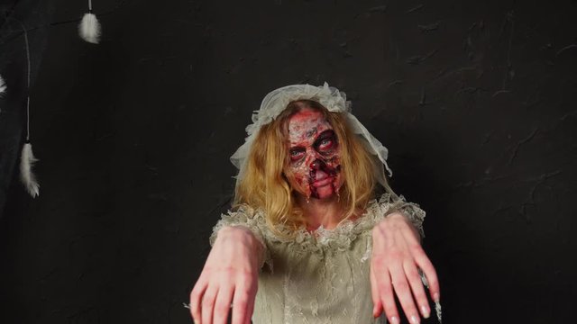 Young blonde woman wearing professional Halloween makeup playing creepy spooky dead wide zombie bride in wedding dress