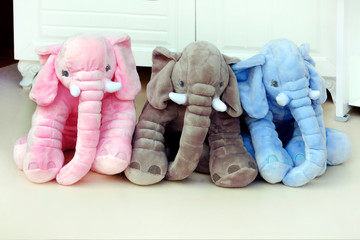 Three multi-colored plush elephants stand on the floor in a shop window against the background of...