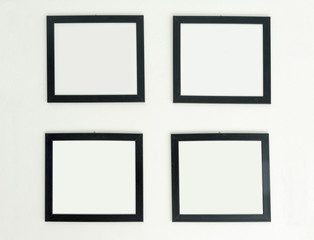 Four identical empty frames hang on white wall