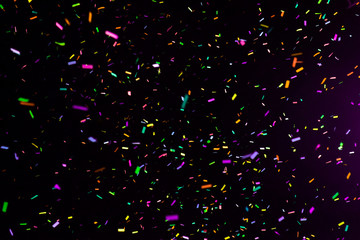 Thousands of confetti fired on air during a festival at night. Image ideal for backgrounds. Multicolor are the confetti in the picture. The sky as background is black. Hot tonality