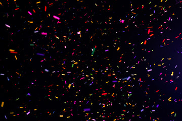 Thousands of confetti fired on air during a festival at night. Image ideal for backgrounds. Multicolor are the confetti in the picture. The sky as background is black. Hot tonality