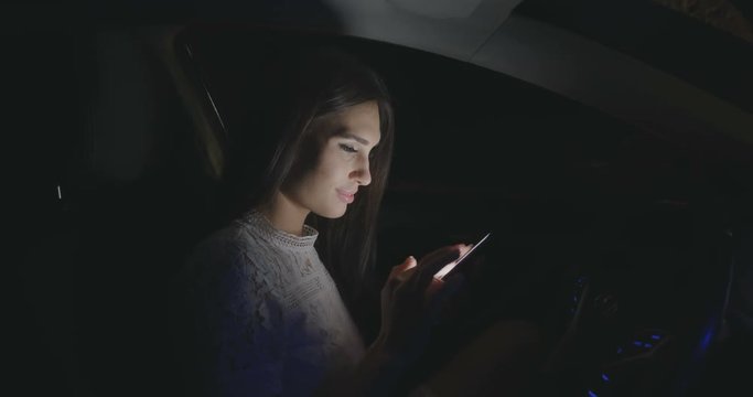 Beautiful woman sitting in the car using smartphone at night.