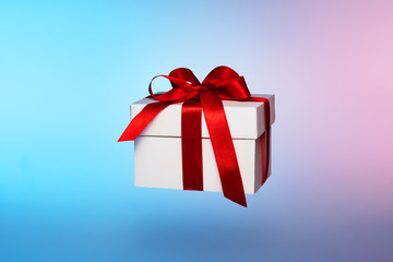 White gift box with red ribbon on colored background.