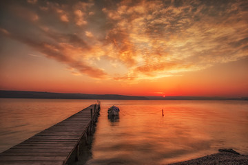 Fototapeta na wymiar Amazing sunset/sunrise at a shore with wooden pier and fishing boat