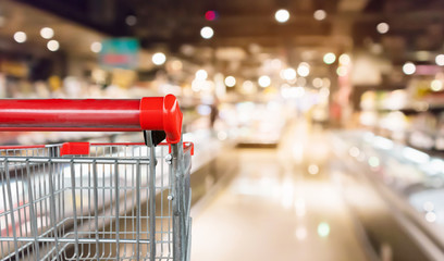 Empty red shopping cart with abstract blur supermarket discount store aisle and product shelves...
