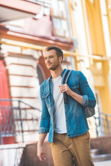 Fototapeta premium attractive young tourist with backpack walking by street and looking away