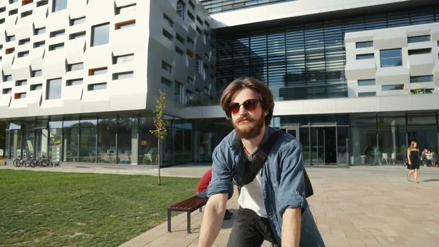 Caucasian man in good shape riding a bike near white modern building, outdoor shot on bright, autumn day