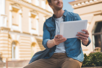 cropped shot of handsome young man using tablet on street