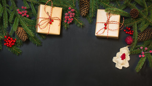 Christmas holiday background - tree, gifts, holly berries and decoration on black chackboard. Holiday card with copy space. Top view.