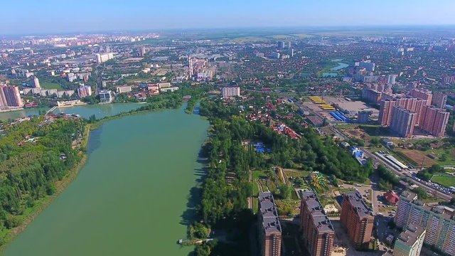 Aerial footage over city Krasnodar River Kuban and Central Park view from top, Krasnodar summer green trees bridge, multi houses skyline visible in distance. Descend green park and birds flying away.