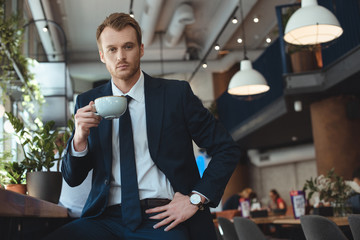 portrait of stylish businessman in suit with cup of coffee having coffee break in cafe