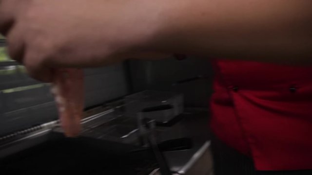 Cook placing a piece of seasoned chicken meat from the borad on the grill in restaurant kitchen