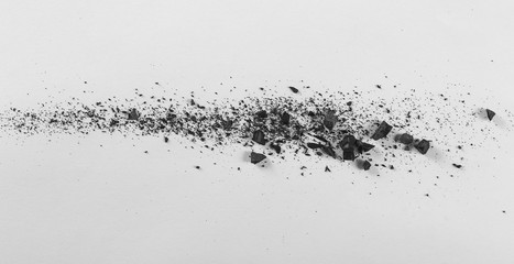 Black charcoal chunks with dust on white paper background and texture