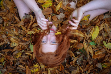 Schönes sexy reizendes junges Mädchen, das auf goldenem Herbstlaub liegt, bedeckt mit bunten herbstlichen Blättern, im Park, mit freundlichem Lächeln im Gesicht.