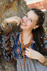 Happy smiling indie style woman with dreads, dressed in boho style ornamental dress outdoor