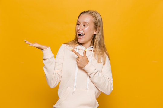 Photo of european school girl with dental braces holding copyspace at palm, isolated over yellow background