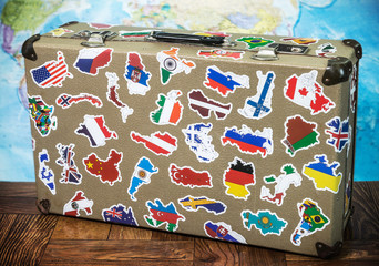 old suitcase with country flag stickers from traveling around the world on the floor. World map background