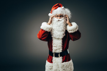 cheerful santa claus in costume holding hands near beard isolated on grey background