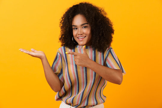 Happy young african cute girl posing isolated over yellow background pointing to copyspace.