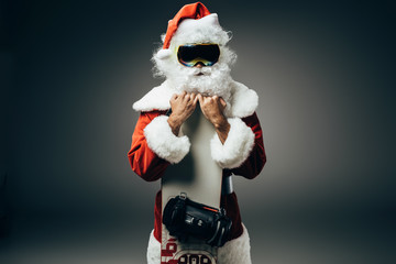 santa claus in ski mask standing with snowboard isolated on grey background