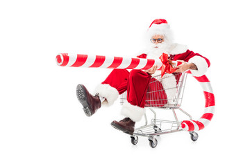 santa claus holding big striped christmas stick in trolley isolated on white background