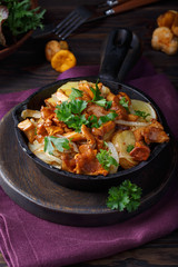 Fried chanterelle mushrooms with potatoes in frying pan on dark background.