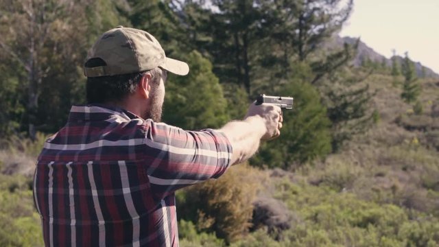 A man shooting a gun outdoors in nature