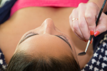 Obraz na płótnie Canvas Makeup artist using brush to apply makeup toattractive young woman eye lids