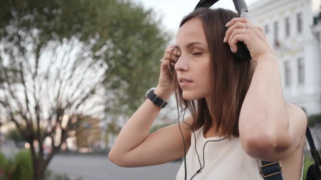 Young woman with smartphone and headphones listening to music on city street.