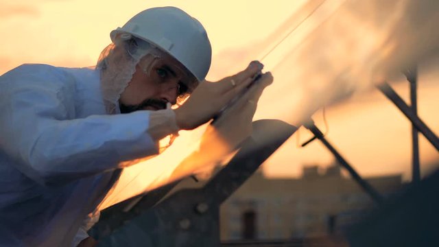 Male expert is wiping glasslike surface of a solar module at the sunset